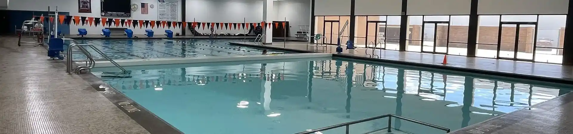 A spacious indoor swimming pool with a flags in the background.
