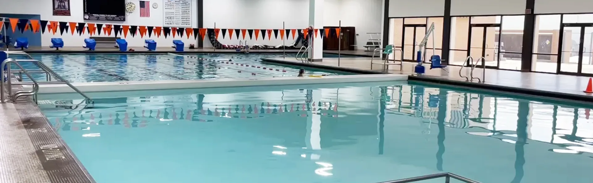 A spacious indoor swimming pool with a flags in the background.